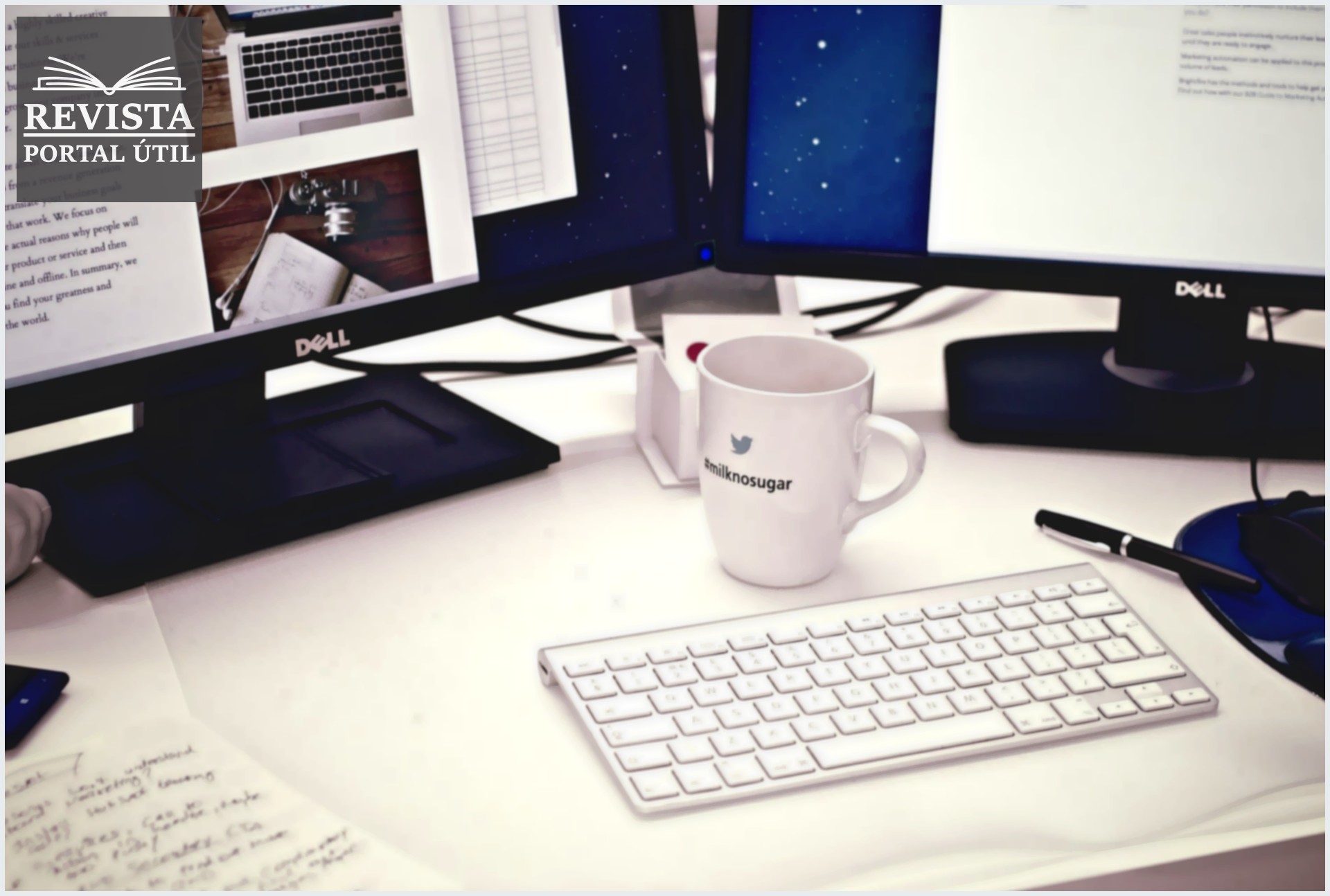 Mesa de escritório com um teclado, dois monitores e uma xicara