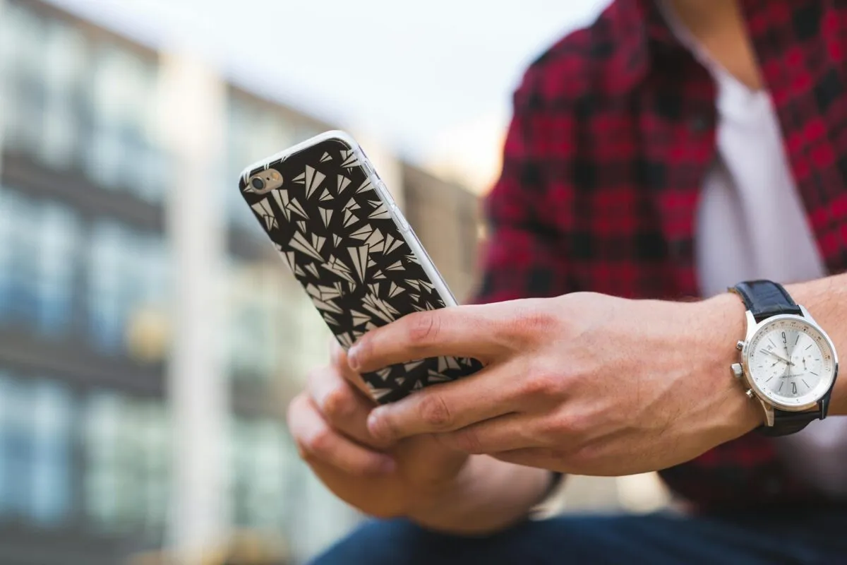 Homem segurando um smartphone com capa estilizada em um ambiente urbano.