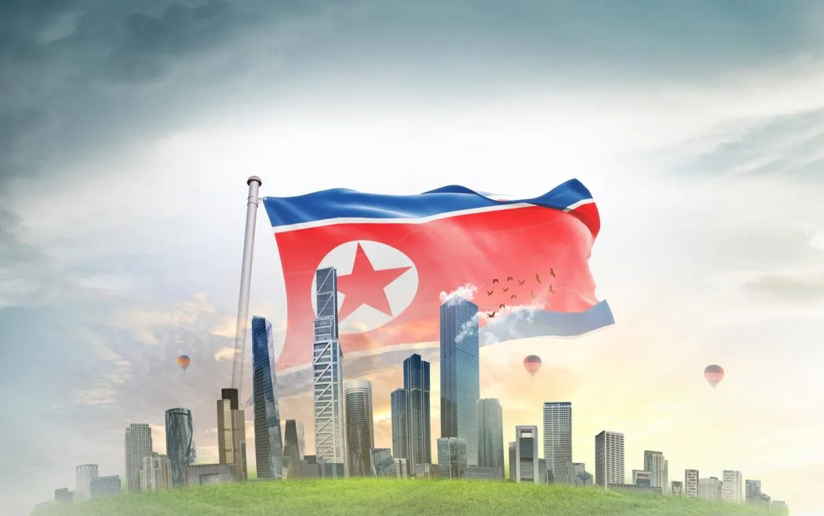 Bandeira da Coreia do Norte tremulando em um mastro diante de arranha-ceus, com baloes e ceu ao entardecer