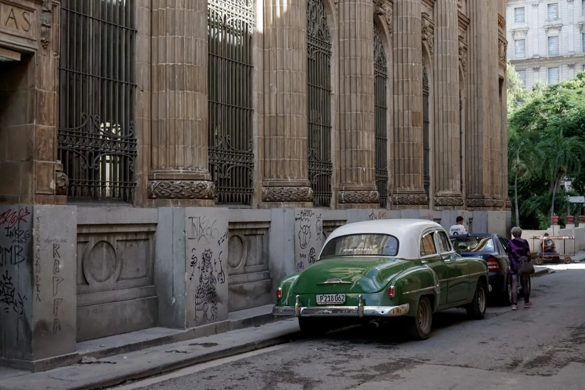 Carro antigo verde estacionado em rua de pedra de Havana, ao lado de prédio colonial com colunas e grades de ferro