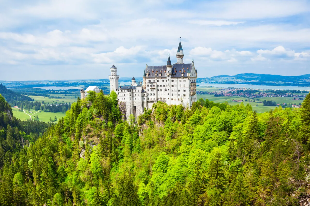 Castelo de Neuschwanstein no alto de uma colina coberta de floresta, com a paisagem verde da Baviera ao fundo