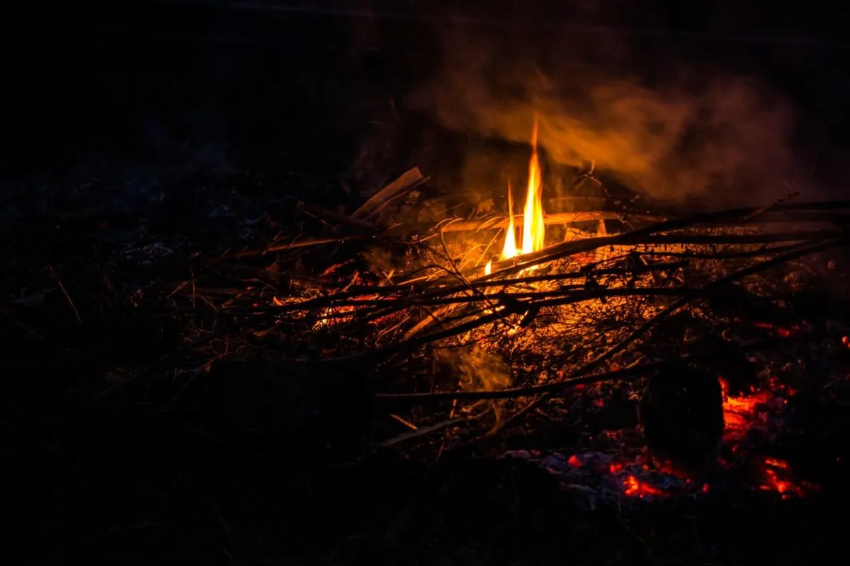 Fogueira acesa no escuro, com chamas alaranjadas, galhos e brasas ao redor durante a noite