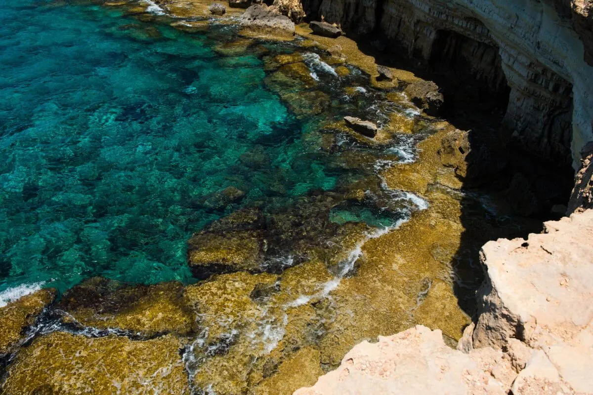 Águas turquesa cristalinas junto a falésias e rochas calcárias na costa da ilha de Chipre, no Mar Mediterrâneo