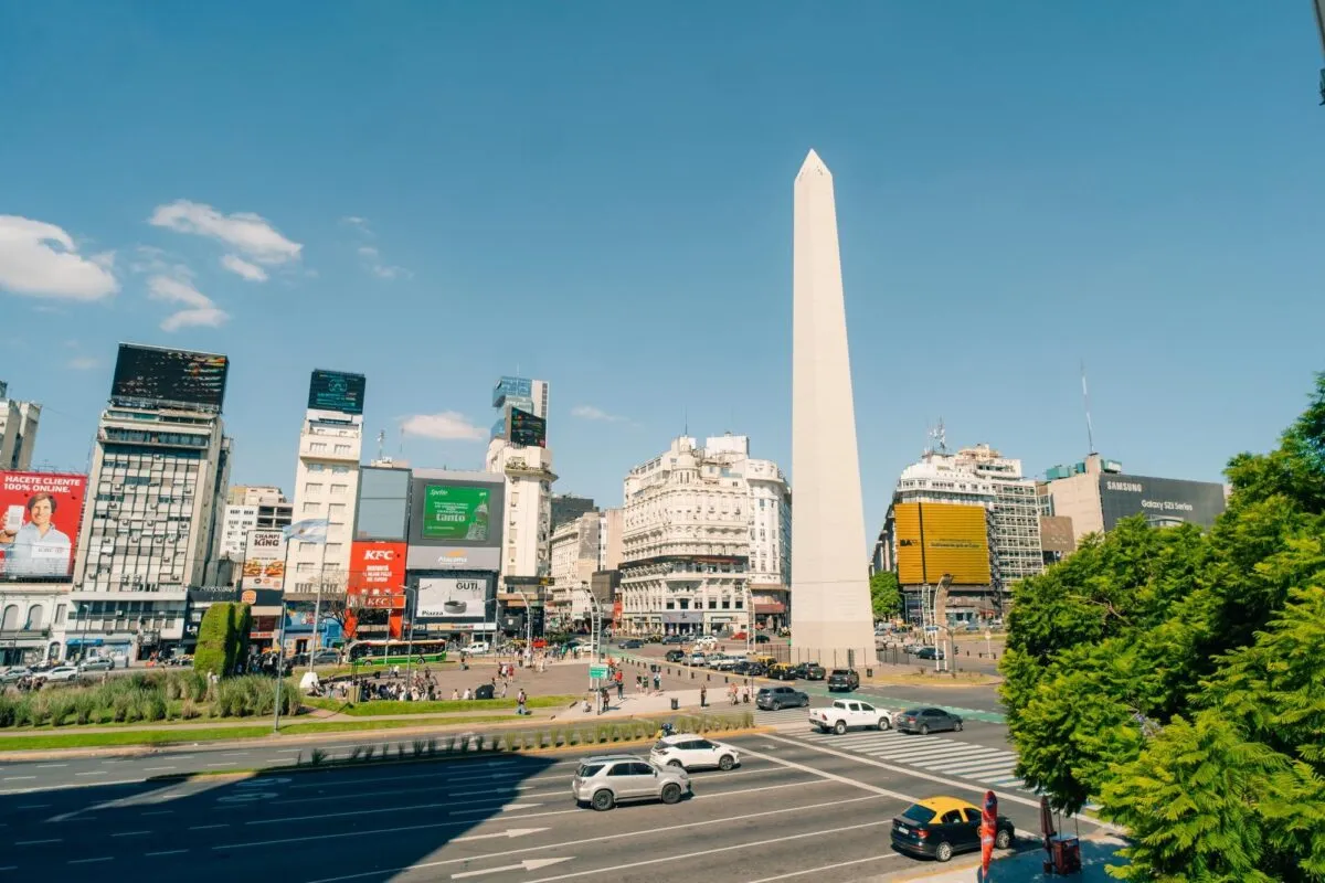 Obelisco de Buenos Aires no centro da Avenida 9 de Julho, com prédios, carros e céu azul ao fundo, na Argentina.