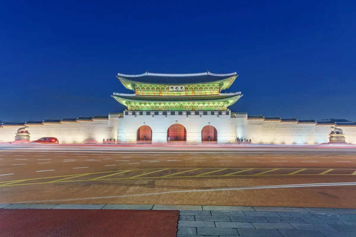 Portão tradicional coreano iluminado ao anoitecer, com muralhas de pedra e céu azul profundo, em Seul
