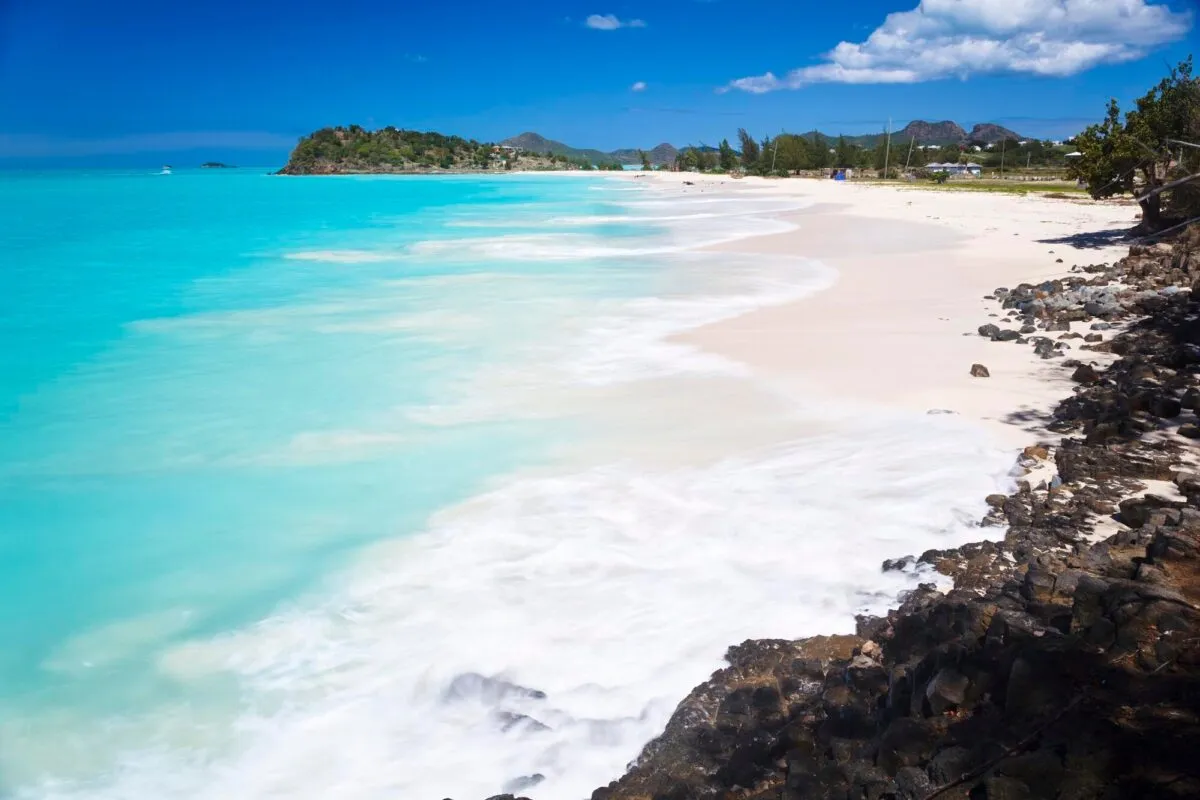 Praia de areia clara e mar azul-turquesa em Antígua, no Caribe, sob céu com poucas nuvens