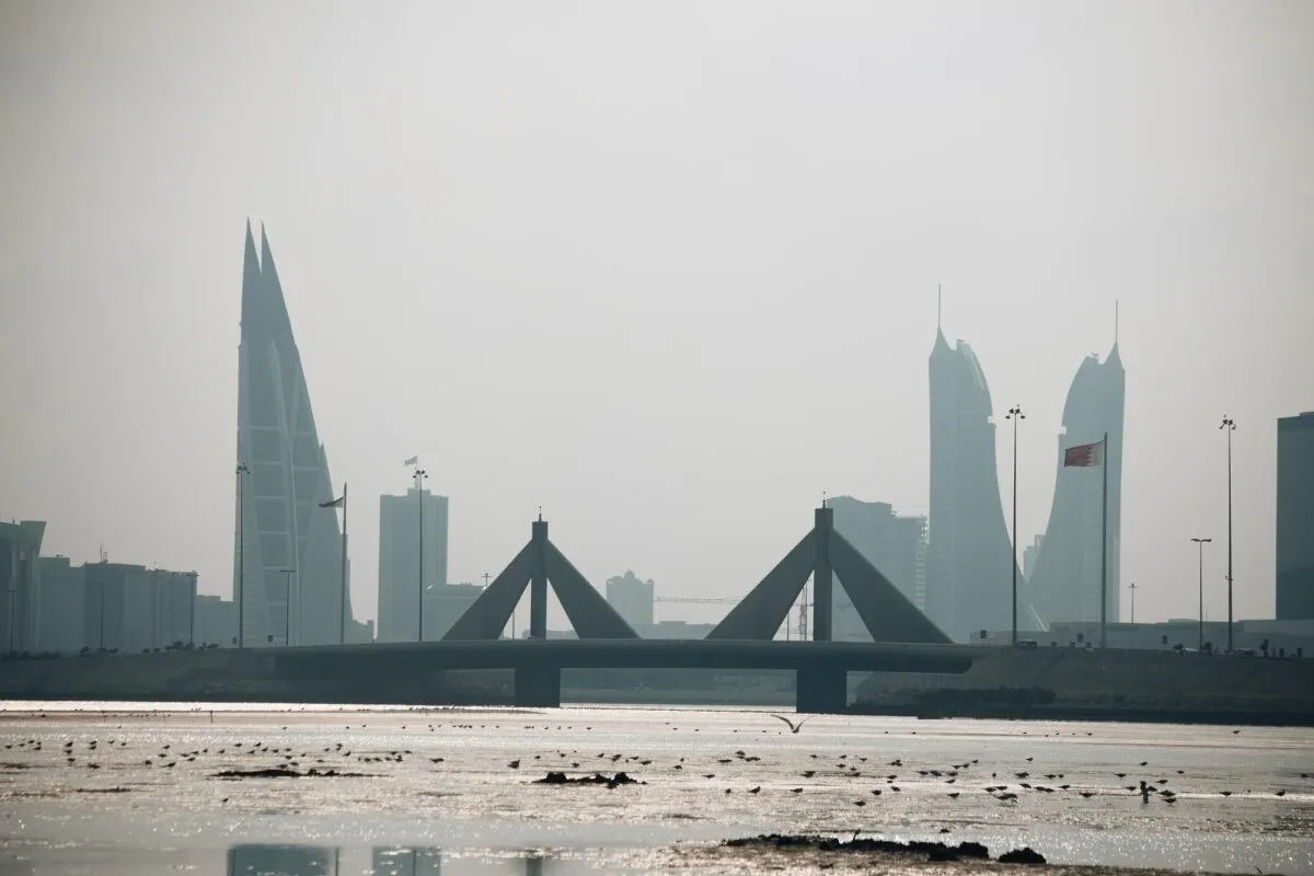 Vista da orla de Manama, no Bahrein, com o Bahrain World Trade Center, torres modernas, uma ponte e aves na maré baixa