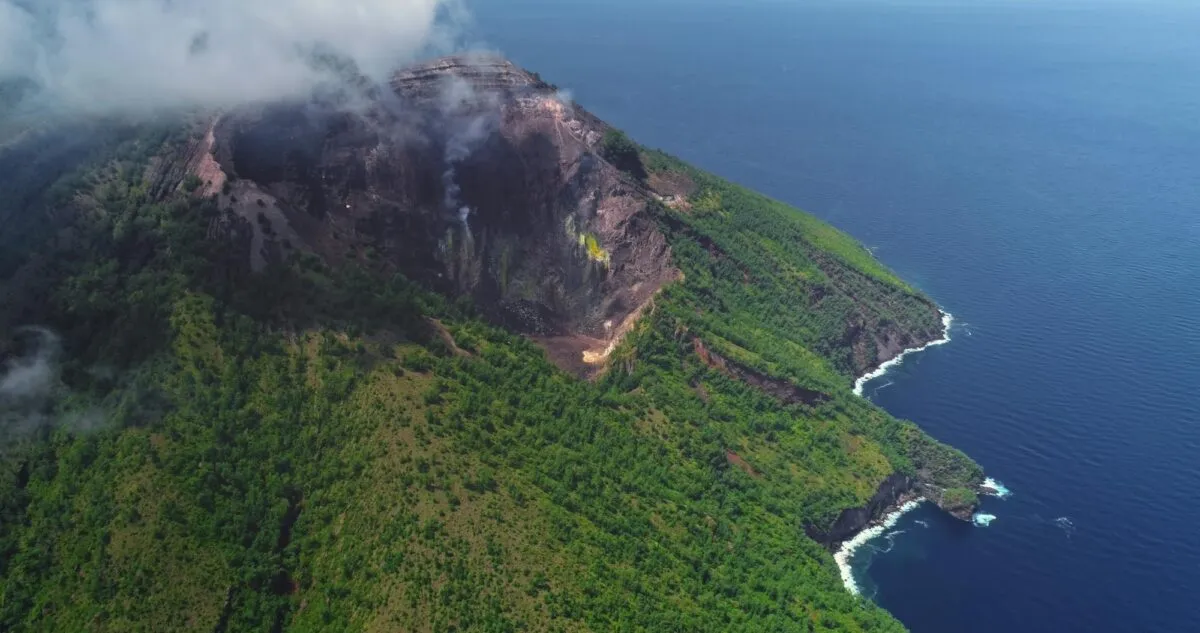 Vista aérea da cratera fumegante de um vulcão ativo na Indonésia, parcialmente coberto por nuvens