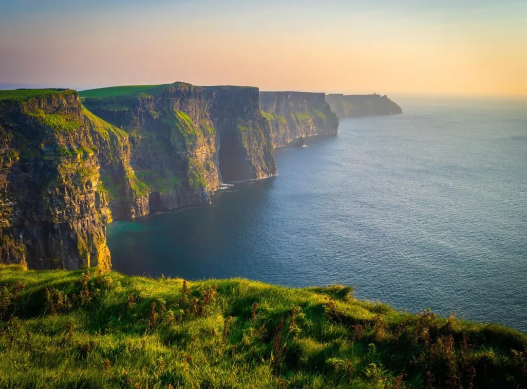 Falésias de Moher cobertas de grama verde sobre o oceano Atlântico, ao pôr do sol, na costa oeste da Irlanda