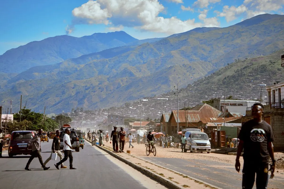 Rua movimentada de uma cidade africana em região montanhosa, com pessoas, bicicletas, veículos e montanhas ao fundo