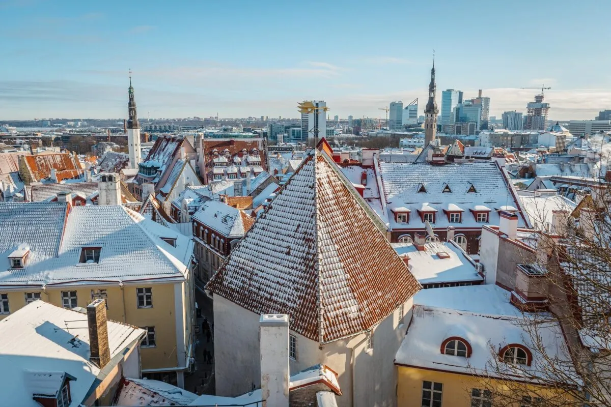 Telhados medievais nevados do centro histórico de Tallinn, com torres de igreja e a skyline moderna da capital da Estônia ao fundo