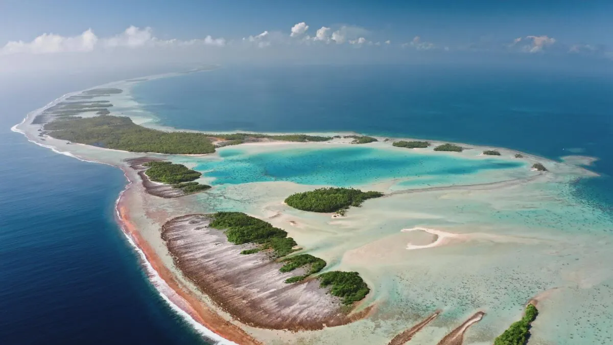 Vista aérea de um atol de coral em formato de anel, cercando uma lagoa de água turquesa no oceano aberto