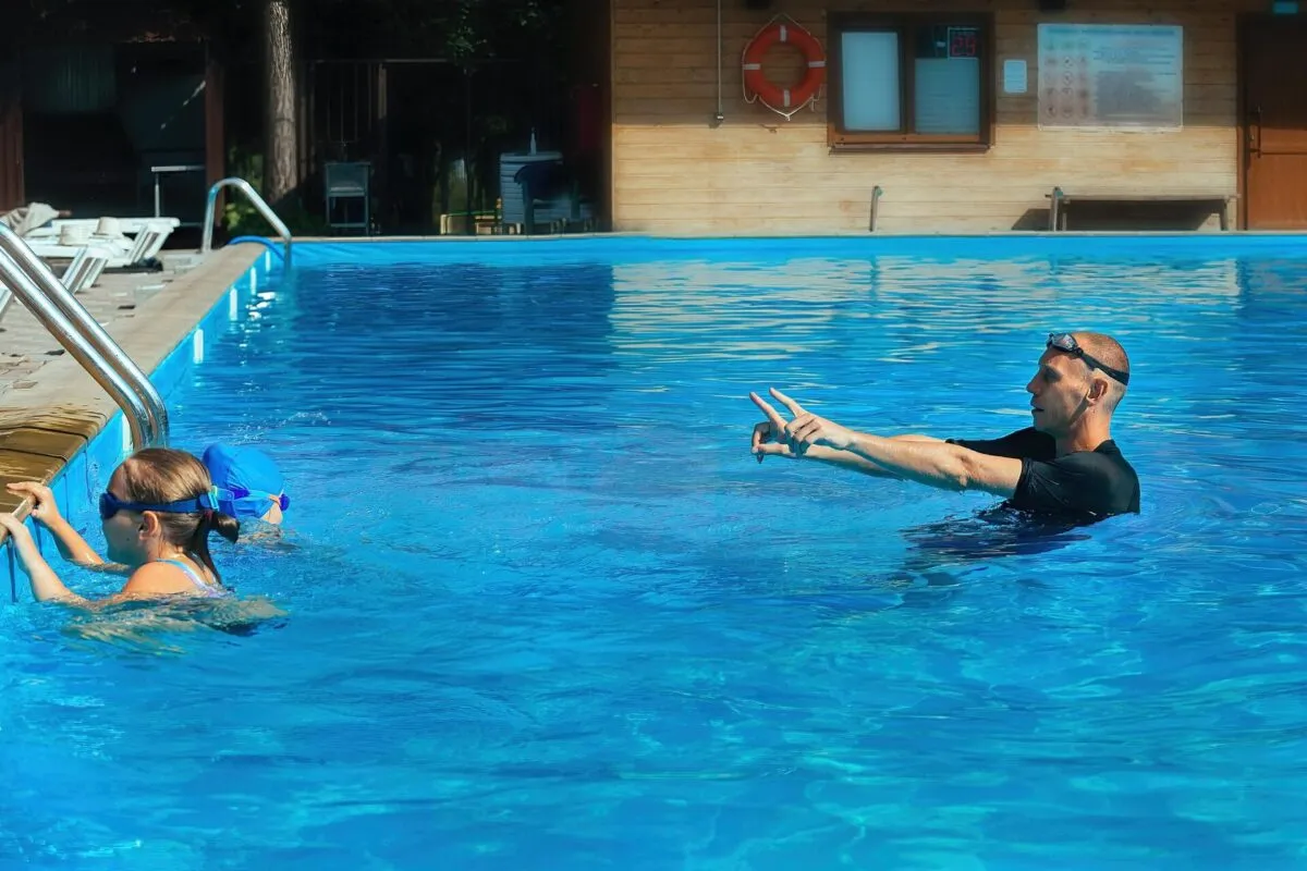 Instrutor de natação em um fundo de piscina azul, orientando duas crianças.
